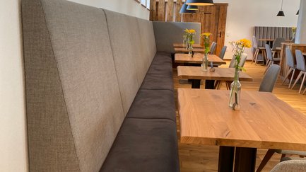 Die Innenansicht eines einladenden Lokals zeigt moderne Tische, gepolsterte Sitzbänke und eine warme, freundliche Atmosphäre.