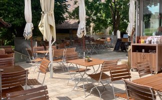 Sonnige Terrasse eines Restaurants, bestückt mit Tischen und Stühlen, bereit für Gäste, die das schöne Wetter genießen wollen.