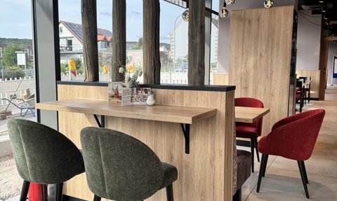 Gemütliche Sitzgelegenheiten in einem Café, das durch große Fenster und natürliche Materialien einladend wirkt.