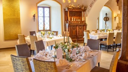 Im Rittersaal erstrahlen gedeckte Tische in warmem Licht, bereit für ein festliches Dinner mit stilvollem Ambiente.