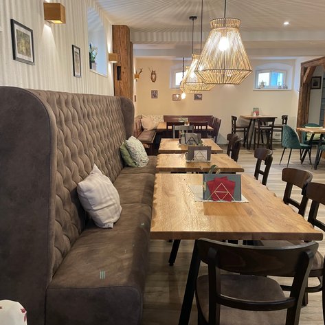 Ein gemütlicher Café-Bereich mit einer gepolsterten Bank, Holztischen, eleganten Stühlen und warmem Licht von modernen Lampen.