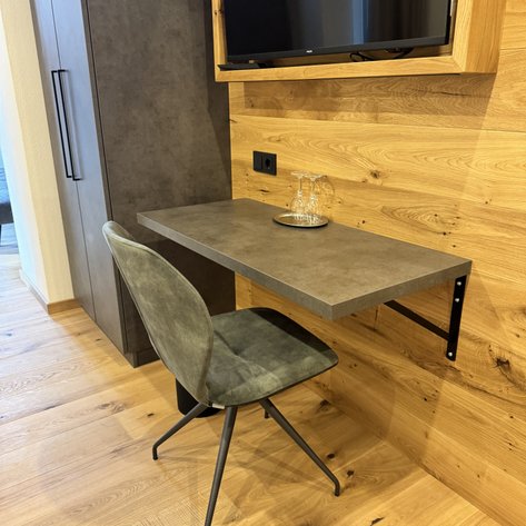 Ein moderner Schreibtisch in einer gemütlichen Ecke, begleitet von einem eleganten Stuhl und einem TV darüber.
