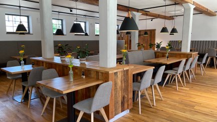 Stilvolle Tische und Stühle aus Holz sind in einem modernen Essbereich angeordnet, geschmückt mit frischen Blumenvasen.