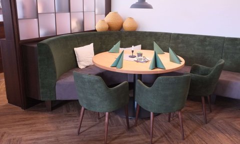 Die grüne Vollpolsterbank mit bunten Kissen und die hölzernen Tische sind perfekt für gesellige Abende in diesem modernen Restaurant.