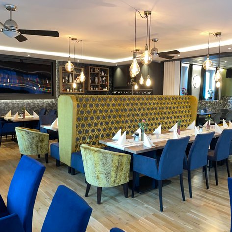 Elegantes Restaurant mit blauen Stühlen und einer dekorativen, goldfarbenen Sitzbank im Hintergrund.
