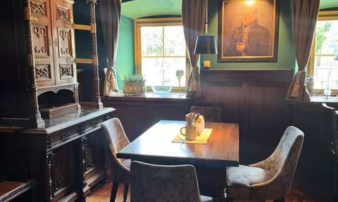 In einem traditionell gestalteten Raum stehen ein Tisch und Stühle, während ein Fenster den Blick nach draußen freigibt.