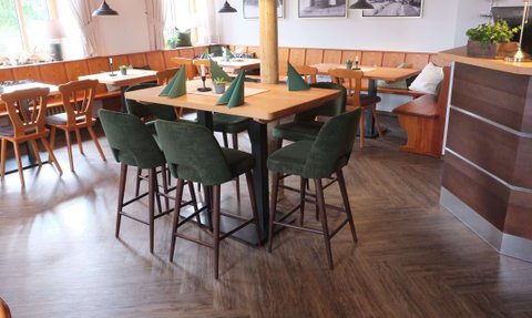 Ein einladender Restaurantbereich mit Holzstühlen, grünen Barhockern und eleganten Tischen, die auf eine gemütliche Atmosphäre hinweisen.