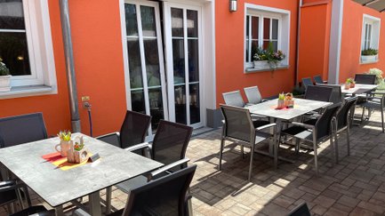 Gemütliche Terrasse eines Lokals, mit eleganten Stühlen und Tischen bereit für Gäste.