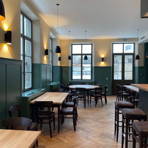 Helles, klassisches Restaurant mit Holzstühlen und großen Fenstern, das eine einladende Atmosphäre schafft.