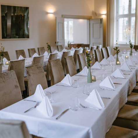 Ein eleganter Speisesaal mit einem langen Tisch, der für eine festliche Veranstaltung gedeckt ist, umgeben von bequemen Stühlen.