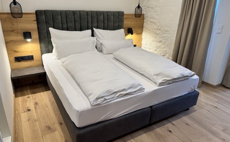 Ein modernes Schlafzimmer mit einem großen Doppelbett, umgeben von warmen Holztönen und sanfter Beleuchtung.