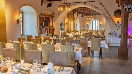 Im Rittersaal erstrahlen gedeckte Tische in warmem Licht, bereit für ein festliches Dinner mit stilvollem Ambiente.