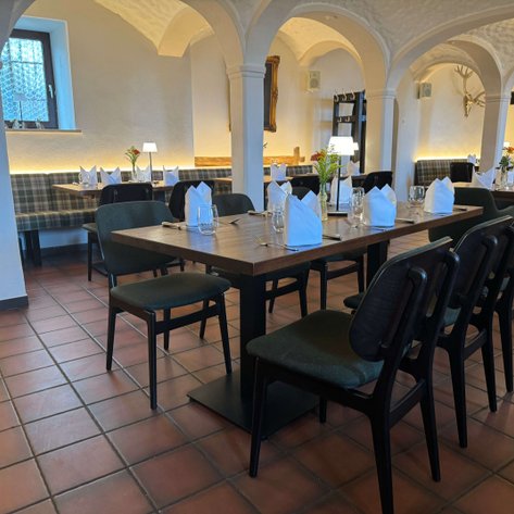 In einem hell erleuchteten Restaurant mit Holztischen und eleganten Stühlen sind Tischdecken und Gläser sorgfältig gedeckt.
