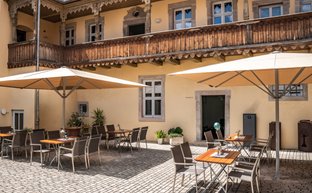 Ein gemütlicher Innenhof mit Tischen und Stühlen unter großen Sonnenschirmen, umgeben von historischen Gebäuden.