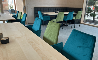 Ein heller, einladender Innenraum mit modernen Holztischen und Stühlen in lebendigen Farben, perfekt für gesellige Zusammenkünfte.