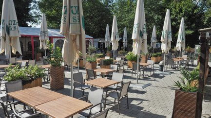 Eine Ansicht eines einladenden Außenbereichs mit zahlreichen Tischen und Stühlen sowie schattenspendenden Sonnenschirmen.