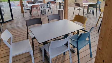 Auf der Terrasse des Cafés warten bunte Stühle und Tische auf Gäste, die die entspannte Atmosphäre im Freien genießen möchten.