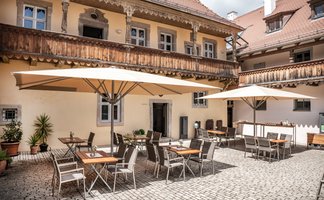 Ein gemütlicher Innenhof mit Tischen und Stühlen unter großen Sonnenschirmen, umgeben von historischen Gebäuden.