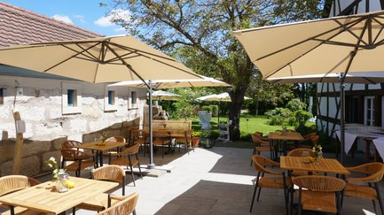 Ein gemütliches Café mit Holzstühlen und Tischen ist von einer schönen Gartenlandschaft umgeben, die zum Entspannen einlädt.