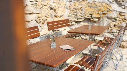 Mehrere Biergartentische und -stühle, umgeben von einer steinernen Wand, die eine einladende Atmosphäre schaffen.