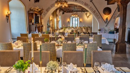 Im Rittersaal erstrahlen gedeckte Tische in warmem Licht, bereit für ein festliches Dinner mit stilvollem Ambiente.