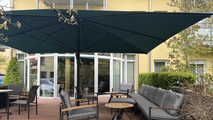 Schwarzer Sonnenschirm, aufgespannt, mit einer Sitzmöglichkeit auf einer Terasse