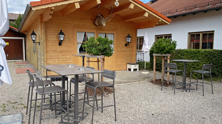 Eine sonnige Terasse mit modernen Stühlen und Tischen neben einem eleganten Holzhaus, das einladend wirkt und zur Entspannung einlädt.