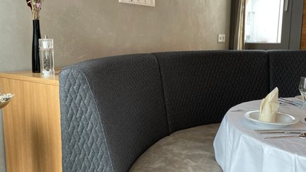 Das Bild zeigt eine gemütliche Nische mit einem grauen Sitzbank und einem schön gedeckten Tisch, ideal für eine Mahlzeit.