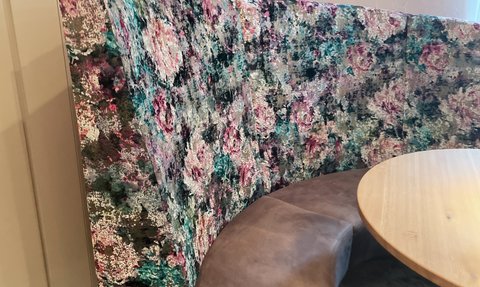 Die gepolsterte Rundbank mit buntem Blumenmuster ergänzt den runden Holztisch im gemütlichen Essbereich.
