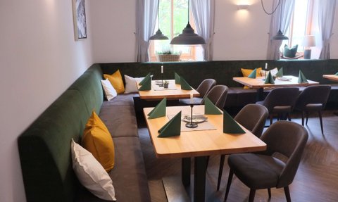 Die grüne Vollpolsterbank mit bunten Kissen und die hölzernen Tische sind perfekt für gesellige Abende in diesem modernen Restaurant.