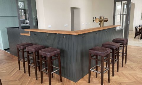 Ein geschmackvoll eingerichteter Barbereich, der eine Holztheke und bequeme Hocker bietet, um Gästen einen angenehmen Aufenthalt zu ermöglichen.