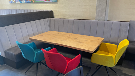Ein stilvoller Tisch aus Holz in einem modernen Restaurant, umgeben von bunten Stühlen in Blau, Rot, Gelb und Schwarz.