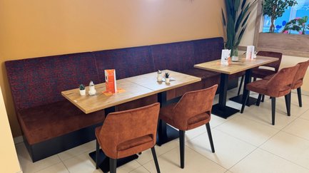 Die gemütliche Café-Ecke zeigt Holztische mit bequemen, samtigen Stühlen, eine entspannte Atmosphäre lädt zum Verweilen ein.