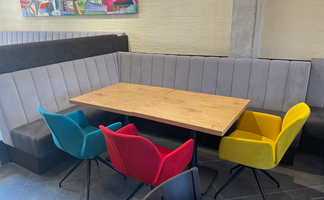 Ein stilvoller Tisch aus Holz in einem modernen Restaurant, umgeben von bunten Stühlen in Blau, Rot, Gelb und Schwarz.