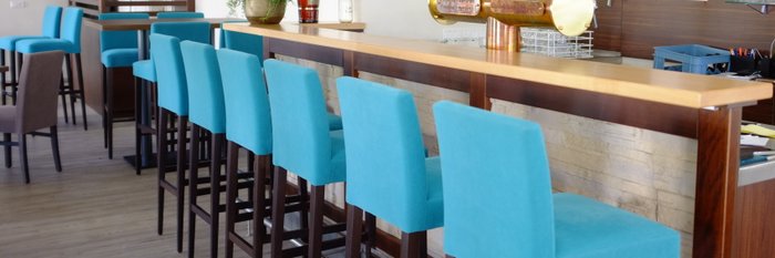 Türkisfarbene Hochstühle vor einer Holzbar