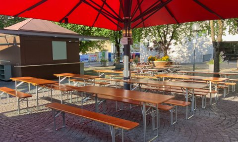 Weitläufige Freifläche mit Biergartentischen und -stühlen unter beschattenden Sonnenschirmen im Herzen von Ingolstadt.