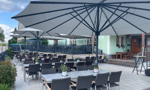 Ein einladender Außenbereich eines Restaurants mit großen Sonnenschirmen, Tischen und Stühlen auf einem hellen Pflasterboden.