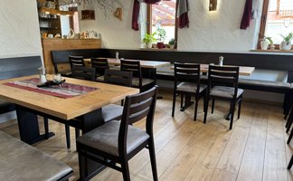 Der Innenraum eines gemütlichen Restaurants zeigt Holztische, Stühle und eine gemütliche Sitzbank.