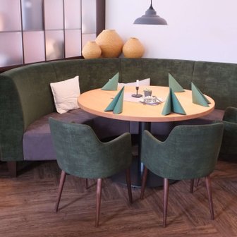 Die grüne Vollpolsterbank mit bunten Kissen und die hölzernen Tische sind perfekt für gesellige Abende in diesem modernen Restaurant.