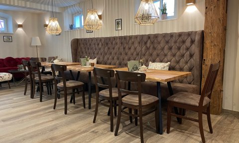 Ein gemütlicher Café-Bereich mit einer gepolsterten Bank, Holztischen, eleganten Stühlen und warmem Licht von modernen Lampen.