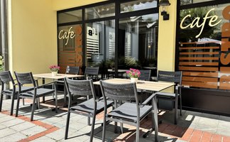 Ein sonniger Cafébereich mit eleganten Stühlen und einem Tisch, der auf eine entspannte Atmosphäre im Freien hinweist.