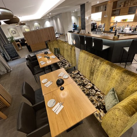 Ein stilvolles Restaurant mit modernen Möbeln, hellem Licht und einem einladenden Barbereich im Hintergrund.