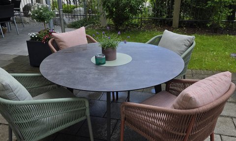 Ein gemütlicher Außenbereich mit einem runden Tisch und farbigen Stühlen, ideal für entspannte Stunden im Freien.