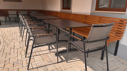 In einem gemütlichen Gartenbereich sind eine Holzbank und mehrere Stühle um einen großen Tisch angeordnet, bereit für Gäste.