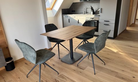 Elegante Stühle aus grauem Stoff um einen modernen Holztisch gruppiert, vor einer modernen Küchenzeile mit dunklen Akzenten.