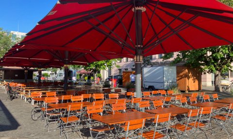 Weitläufige Freifläche mit Biergartentischen und -stühlen unter beschattenden Sonnenschirmen im Herzen von Ingolstadt.