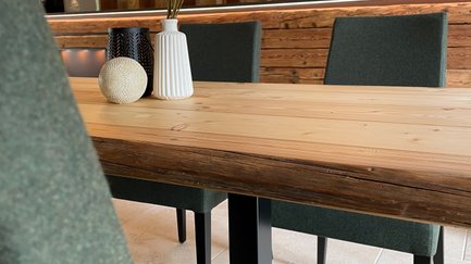 Rustikaler Raum mit massiven Holztischen und bequemen Stühlen mit grünem Bezug.