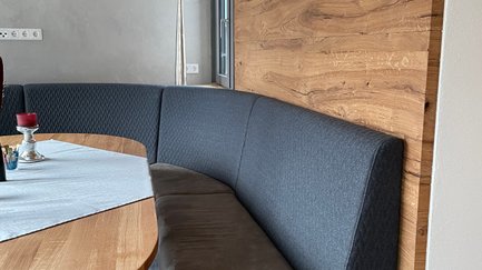 Das Bild zeigt eine gemütliche Nische mit einem grauen Sitzbank und einem schön gedeckten Tisch, ideal für eine Mahlzeit.