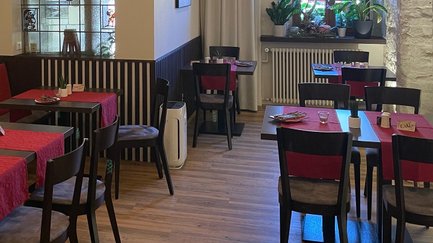 Ein gemütliches Restaurant mit roten Tischdecken und weißem Fußboden, beleuchtet von modernen hängenden Lampen.