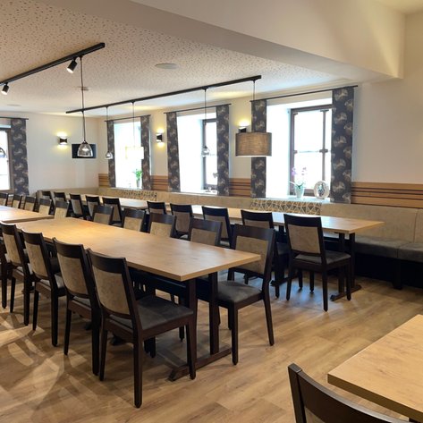 Ein stilvoll gestalteter Raum mit langen Holztischen und eleganten Stühlen, ideal für gesellige Zusammenkünfte oder Veranstaltungen.